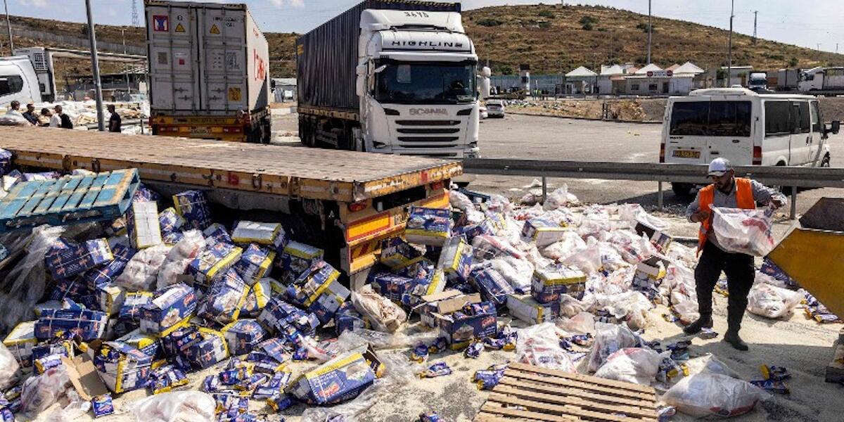 A worker clears spilled goods away from damaged trailer trucks that were carrying humanitarian aid supplies on the Israeli side of the Tarqumiyah crossing with the occupied West Bank on May 13