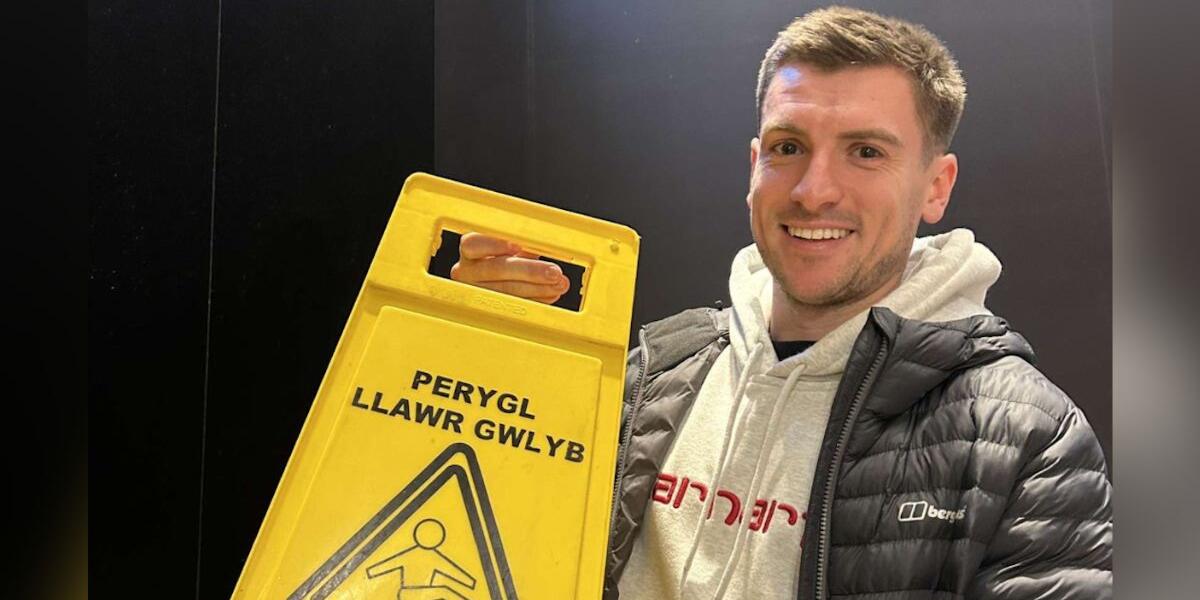 Tom Oliver gydag arwydd Cymraeg