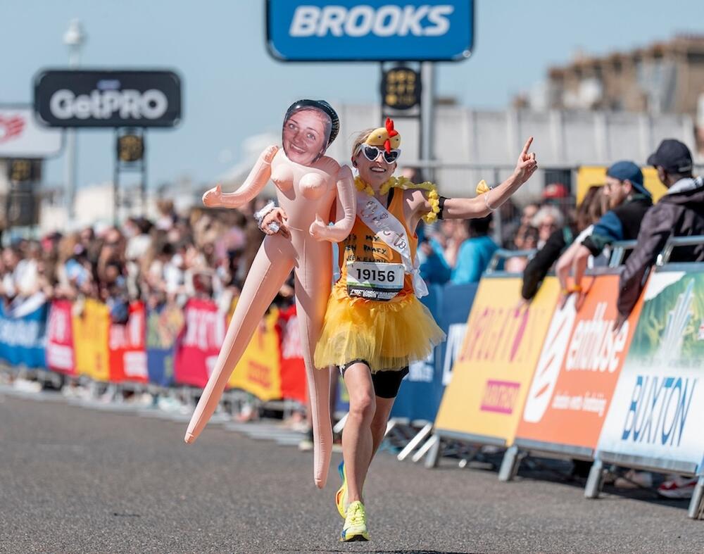 Emily Marchant yn gorffen y marathon gyda dol chwyddadwy (inflatable)